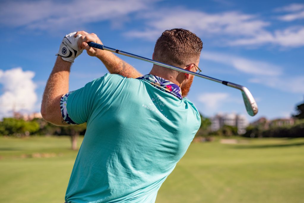 Fit man swings golf club on a golf course.