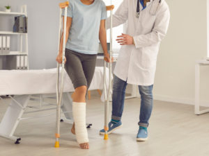 A person walking with crutches and a leg cast with the help of a doctor.