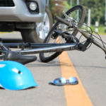 Blue bicycle helmet broken on the street with a bent bicycle and a car.