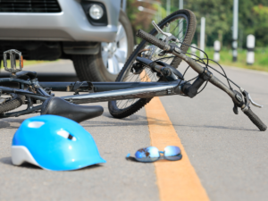 Blue bicycle helmet broken on the street with a bent bicycle and a car.
