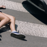 A woman on the ground of a sidewalk with a car nearby.