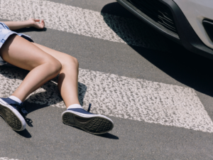 A woman on the ground of a sidewalk with a car nearby.